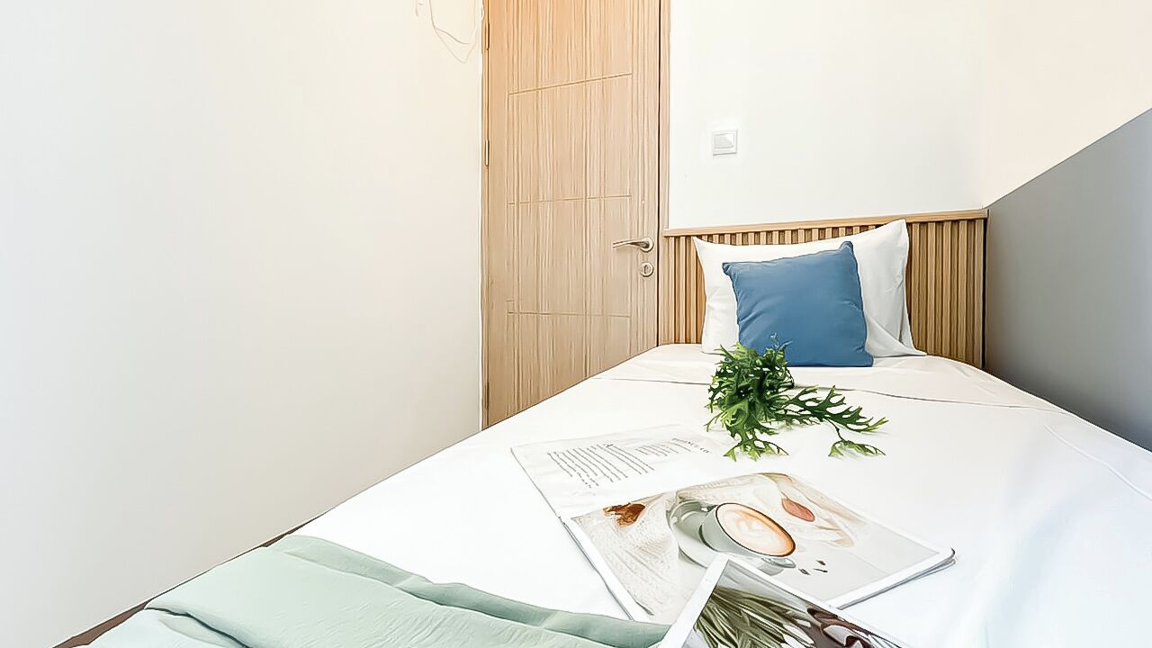 A neatly made bed with a white and blue pillow, a magazine, a cup, and a plant on the bed.