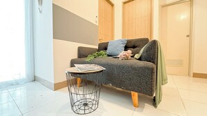 Een moderne woonkamer met een grijze bank, een klein rond tafeltje met een tijdschrift, en een groene plaid.