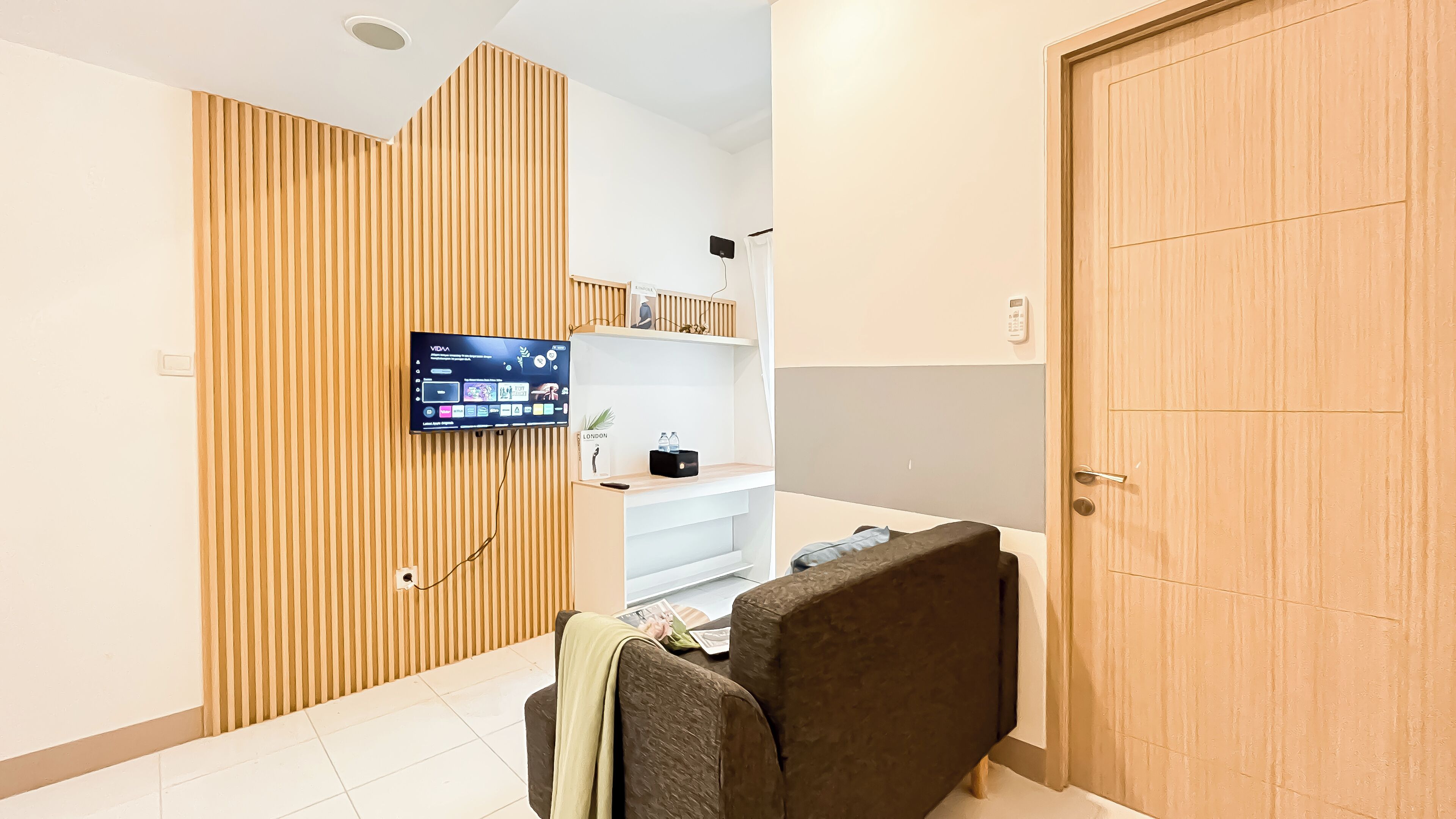 A modern living room with a TV mounted on a wooden panel wall, a sofa, a small table with a tray, and a wooden door.