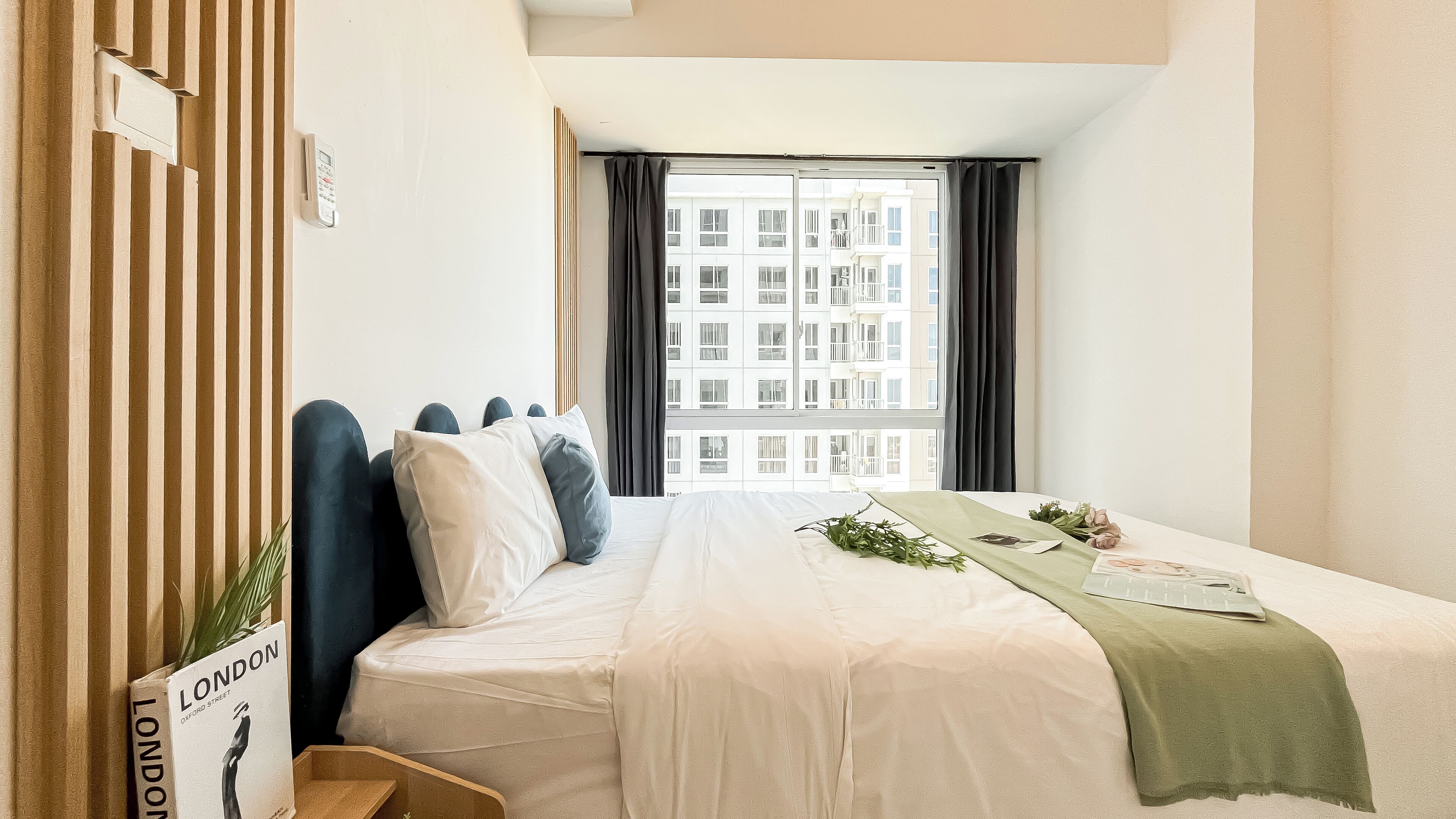 Une chambre d’hôtel avec un lit, une fenêtre avec des rideaux, une table de chevet et une plante.