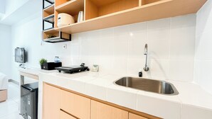 Cozinha moderna com azulejos brancos, pia de aço inoxidável, armários de madeira e bancada com uma balança e uma chaleira.