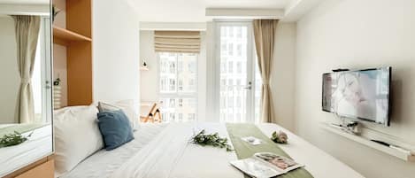 A hotel room with a bed, a television, and a window with curtains.