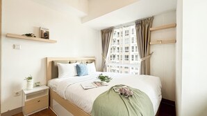 A neatly arranged bedroom with a bed, bedside tables, a window with curtains, and a view of buildings outside. - Modern 2Br At Apartment Tokyo Riverside Pik 2 Near Tokyo Hub (Teluknaga)