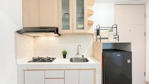 A compact kitchen with a gas stove, a stainless steel sink, and a black refrigerator. - Modern 2Br At Apartment Tokyo Riverside Pik 2 Near Tokyo Hub (Teluknaga)