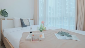 A neatly made bed with a beige bedspread, a small plant, and a framed picture on the bedside table. - Strategic And Spacious 2Br At Capitol Park Residence Apartment (Jakarta)