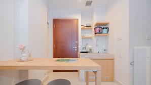 A compact kitchen with a wooden table, two stools, a white refrigerator, and a wooden door. - Strategic And Spacious 2Br At Capitol Park Residence Apartment (Jakarta)