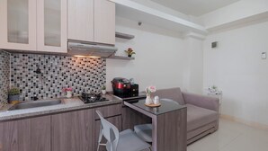 A compact kitchen with a built-in island, a modern stove, and a small dining area with a sofa and chairs. - Strategic 2Br Apartment At Green Pramuka City (Jakarta)