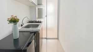 A modern kitchen with a black countertop, stainless steel sink, and a gas stove. There is a white vase with flowers on the counter. - 1Br At Vittoria Residence Apartment Near Puri Indah Mall (Jakarta)