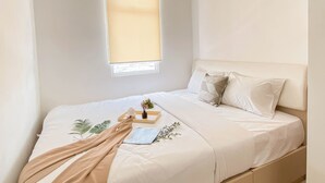 A bedroom with a bed, white bedding, a window with a blind, and a bedside table with a lamp and a tray. - 1Br At Vittoria Residence Apartment Near Puri Indah Mall (Jakarta)