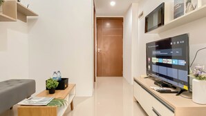 A modern living room with a flat-screen TV, a sofa, a coffee table with a magazine, and a small plant. - 1Br At Vittoria Residence Apartment Near Puri Indah Mall (Jakarta)
