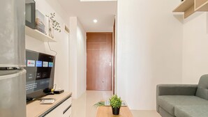 A modern living room with a flat-screen TV, a wooden coffee table, a grey sofa, and a door leading to another room. - 1Br At Vittoria Residence Near Daan Mogot Mall (Jakarta)