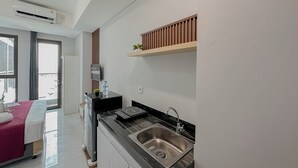 A modern kitchen with a built-in sink, a Bosch refrigerator, and a wooden shelf above the counter. - Simple Studio At The Trans Icon Surabaya Apartment (Surabaya)