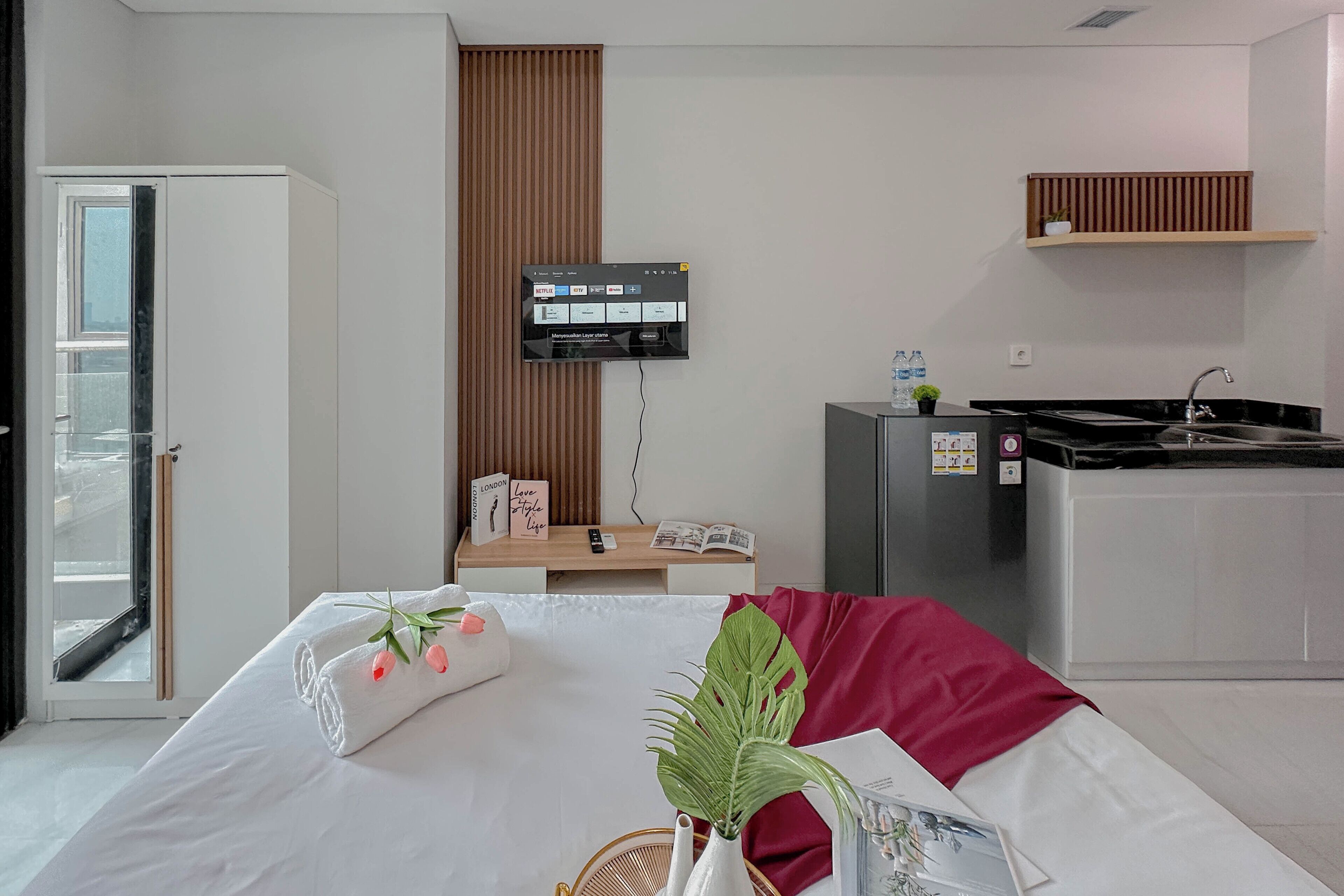 Een hotelkamer met een bed, een aan de muur bevestigde televisie, een kleine kitchenette en een raam met uitzicht.