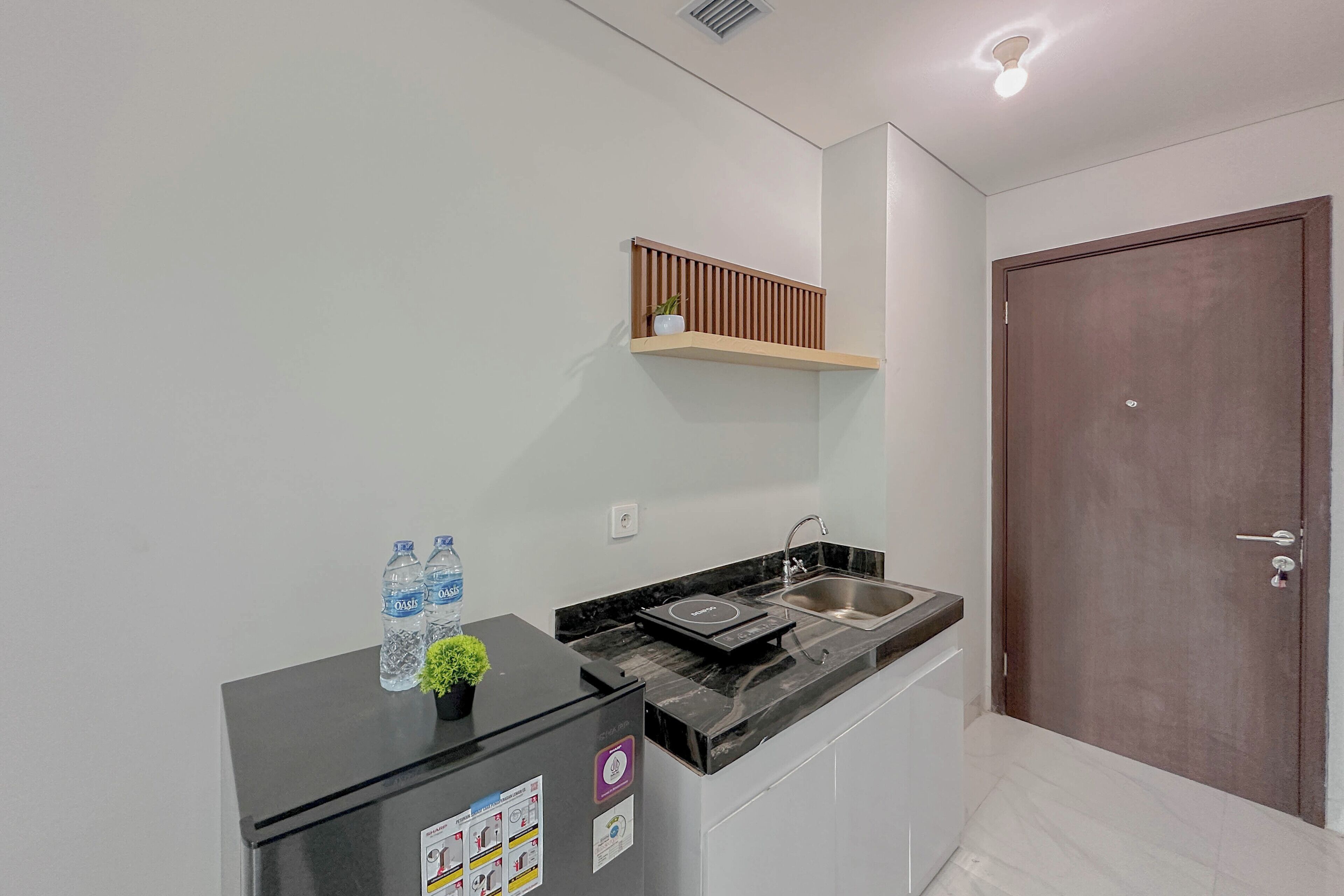 A compact kitchen with a black countertop, a built-in sink, and a wooden shelf above.