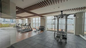 A modern gym with exercise equipment, large windows, and a view of the cityscape. - Simple Studio At The Trans Icon Surabaya Apartment (Surabaya)