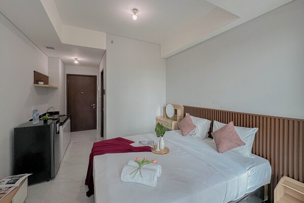 Ein modernes Hotelzimmer mit einem ordentlich bezogenen Bett, einem kleinen Nachttisch, einem Schreibtisch mit Stuhl und einer Tür zu einem weiteren Raum.