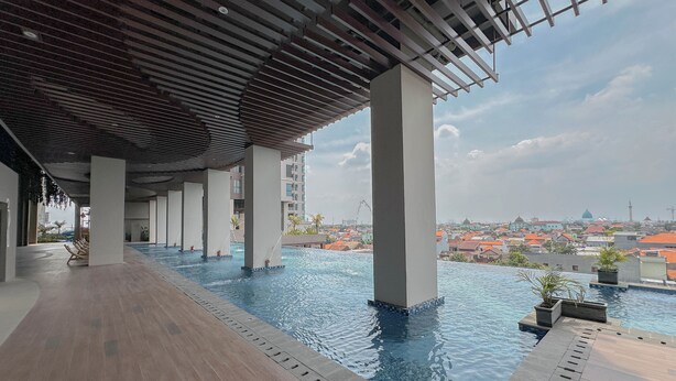 A rooftop infinity pool with a wooden deck and a view of the cityscape. - Simple Studio At The Trans Icon Surabaya Apartment (Surabaya)