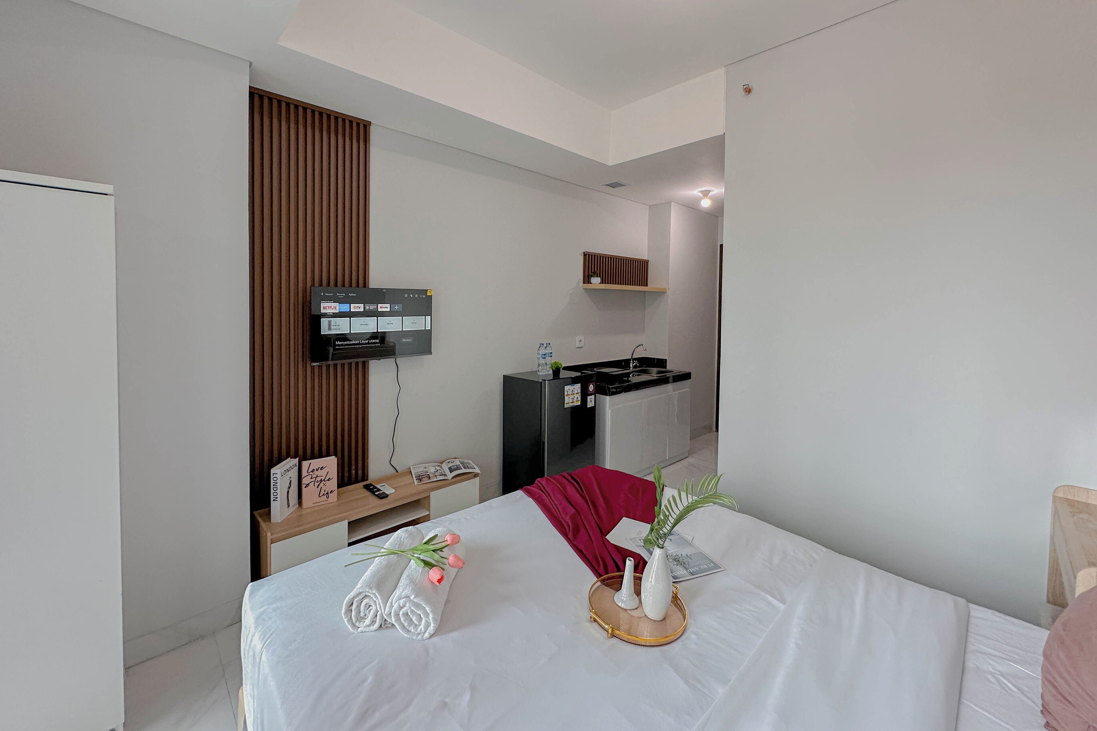 Una habitación de hotel moderna con una cama, un televisor fijado a la pared, una pequeña cocina y un panel de madera.