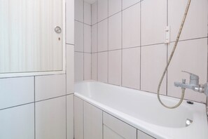 A bathroom with white tiles, a bathtub, a showerhead, and a door with a lock. - Spacious 2Br Near Mall At Grand Kamala Lagoon Apartment (Bekasi)