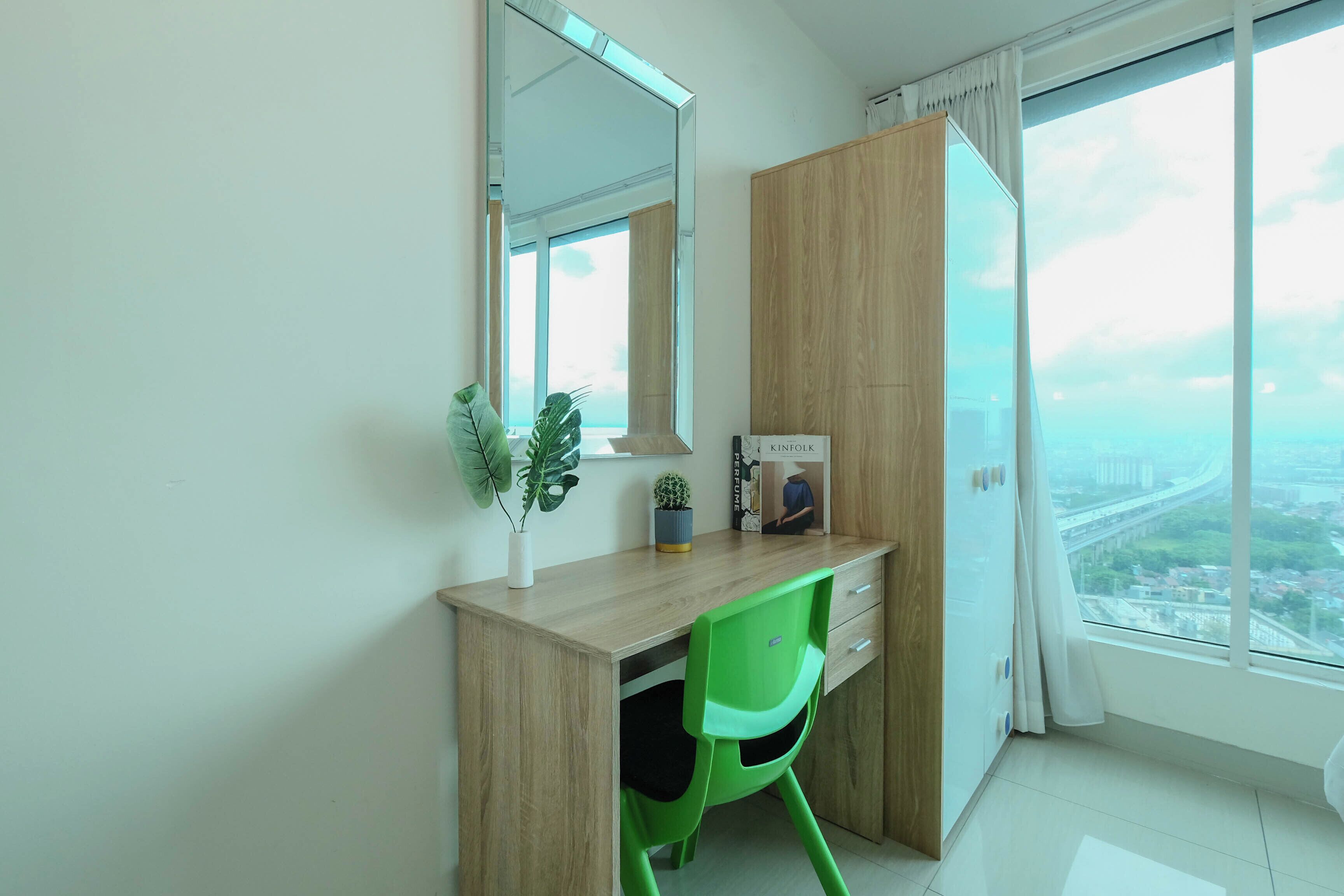 Une chambre moderne avec un bureau en bois, une chaise verte, un grand miroir et une vue sur le paysage urbain, visible à travers une grande fenêtre.