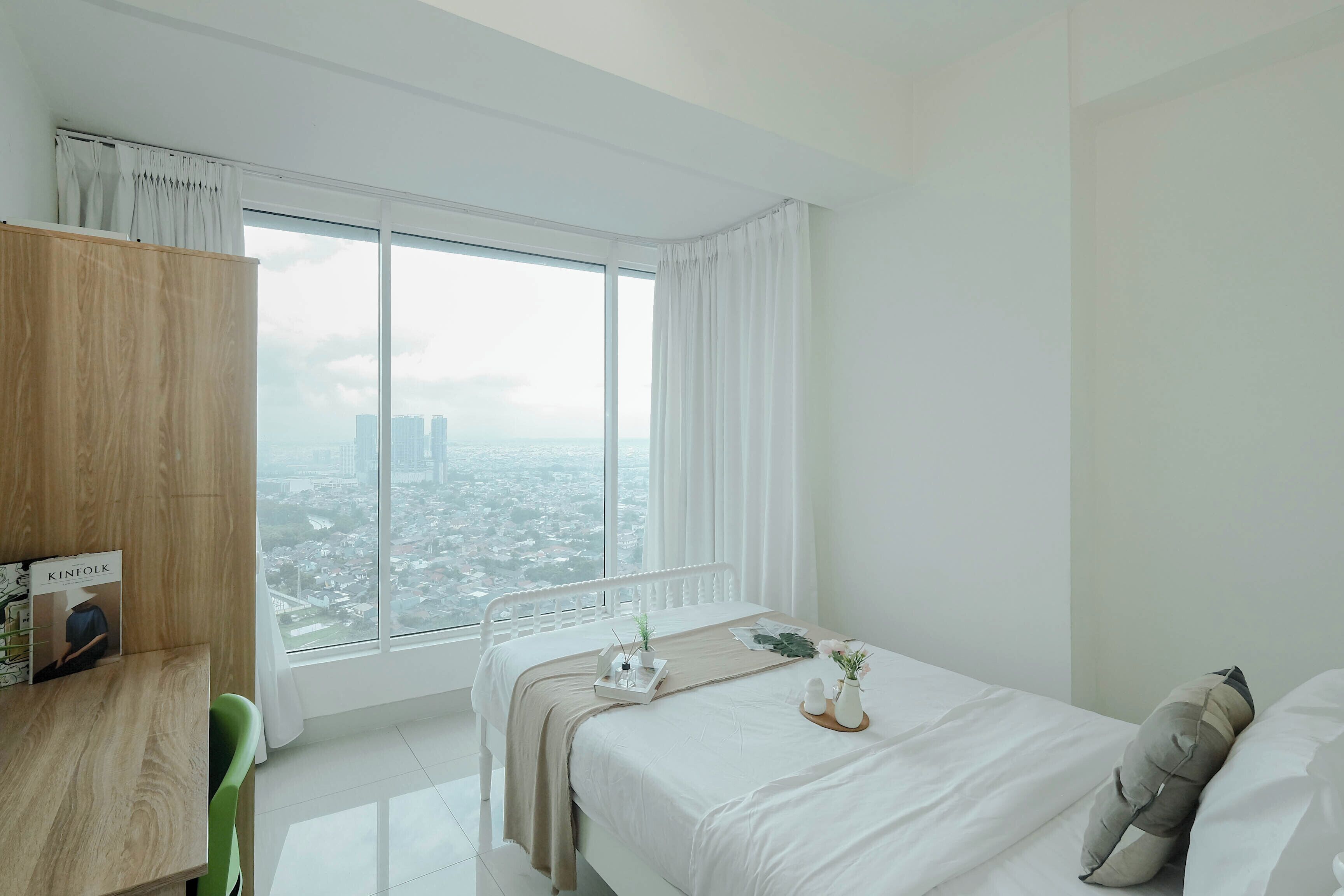 Una habitación de hotel moderna con un ventanal grande, una cama con sábanas blancas, una mesita de noche con una bandeja y vistas a la ciudad.