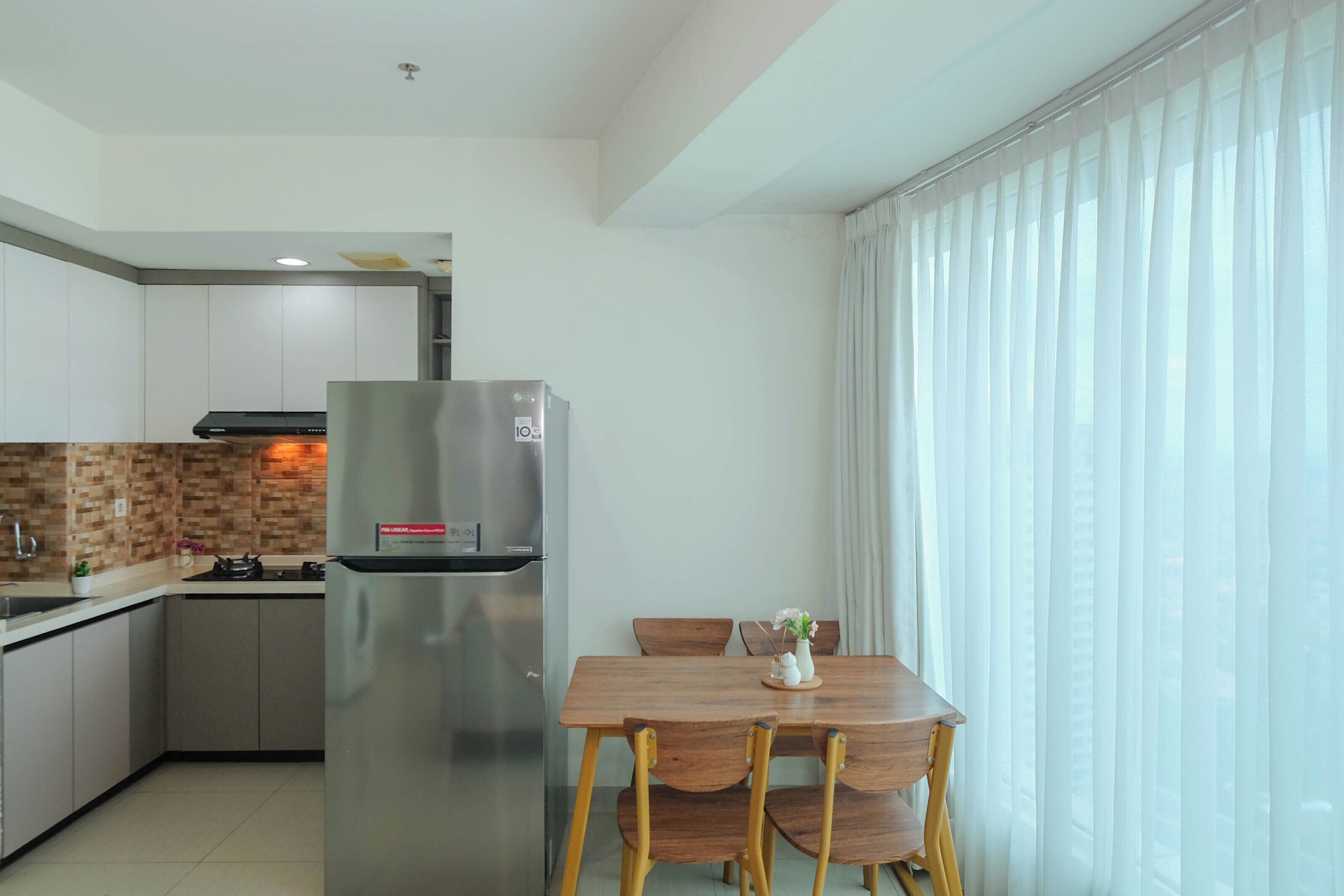 A modern kitchen with a stainless steel refrigerator, wooden dining table, and chairs.