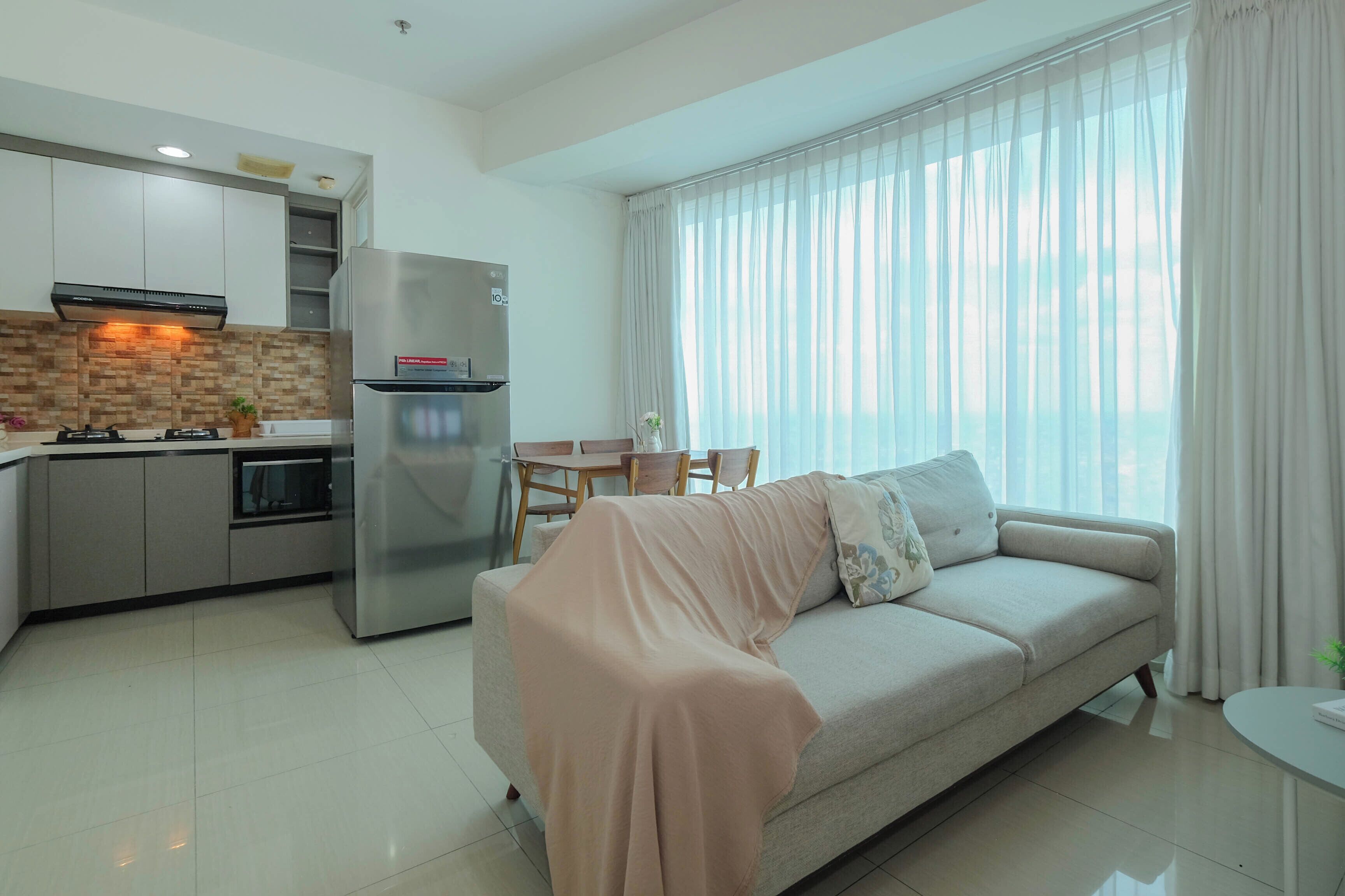 A modern living room with a sofa, a dining table, and a kitchen area with a refrigerator and stove.