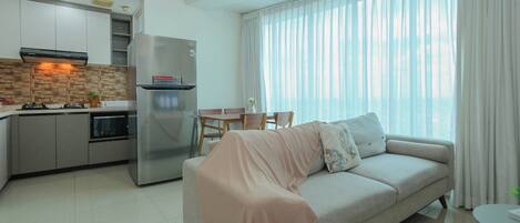 A modern living room with a sofa, a dining table, and a kitchen area with a refrigerator and stove.