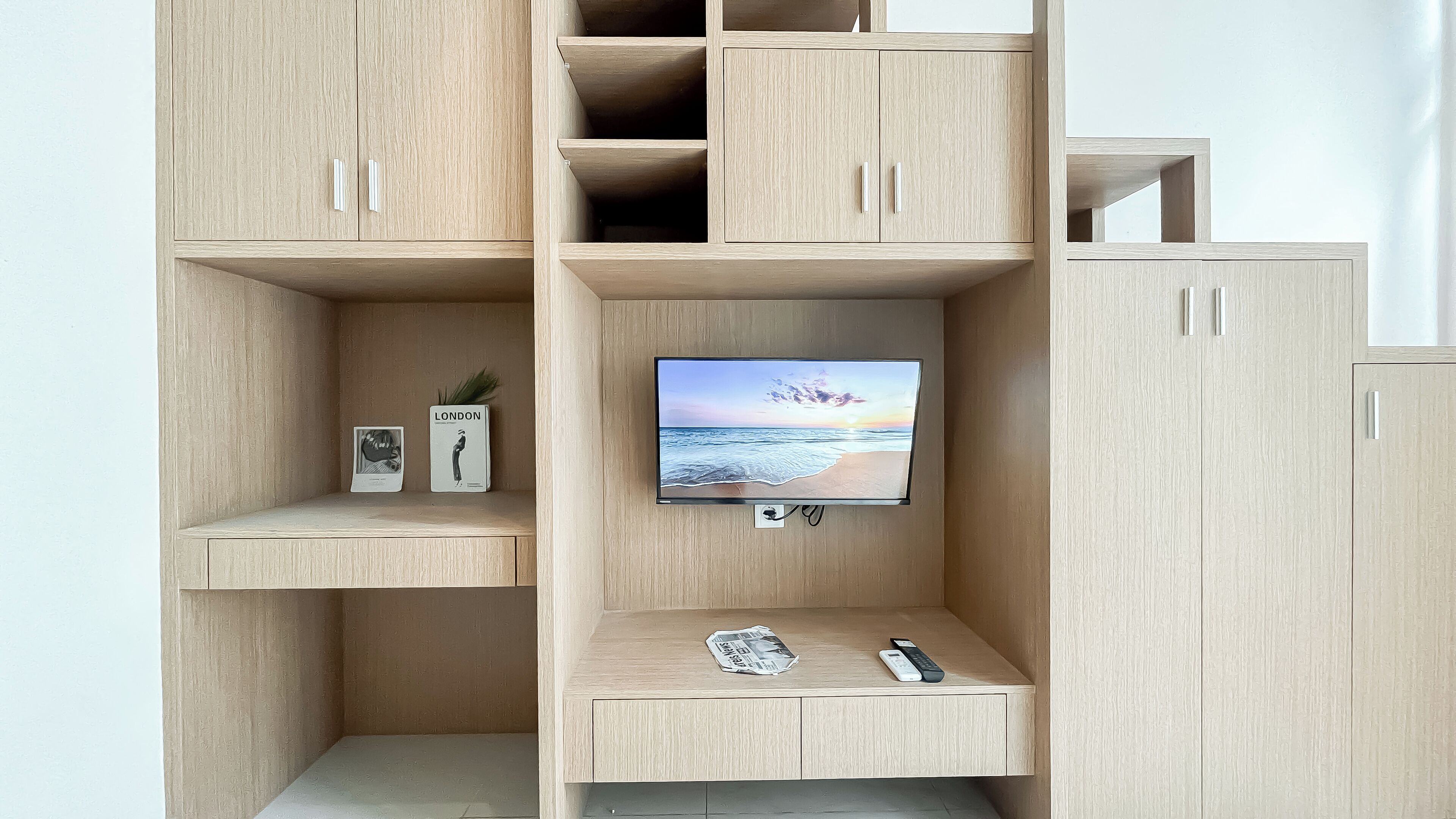 A modern, multi-tiered wooden cabinet with a flat-screen TV mounted on the middle shelf, displaying a beach scene.