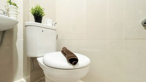 A white toilet with a brown towel on the seat, a potted plant on the tank, and a toilet paper roll. - Nice Look Studio At Apartment Apple 1 Condovilla (Jakarta)