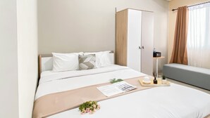 A hotel room with a bed, a bedside table with a lamp, a small plant, and a window with curtains. - Cozy And Best Place Studio Apartment Royal Sentul Park (Bogor)