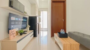 A modern living room with a flat-screen TV mounted on the wall, a wooden coffee table, a grey sofa, and a wooden door. - Restful 1Br Apartment At Vittoria Residence (Jakarta)