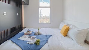 A bedroom with a bed, a window, and a view of a cityscape. - Restful 1Br Apartment At Vittoria Residence (Jakarta)