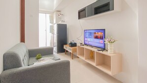 En moderne stue med en grå sofa, et fladskærms TV, et træ sidebord og en lille plante.