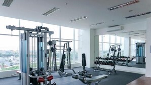 Et rummeligt fitnessrum med forskellig træningsudstyr, store vinduer og udsigt over byen.
