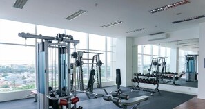 Ein großzügiger Fitnessraum mit verschiedenen Trainingsgeräten, großen Fenstern und Blick auf die Stadt.