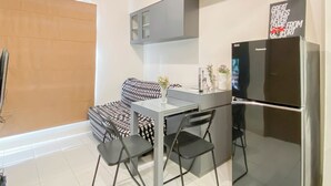 A compact kitchen with a refrigerator, a dining table, and a sofa. - Standard 2Br At Podomoro Golf View Apartment (Gunung Putri)