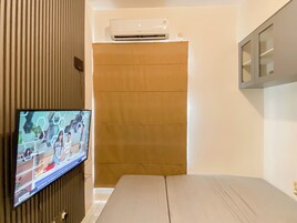 A room with a television displaying a news program, a wall-mounted air conditioner, and a wooden cabinet.