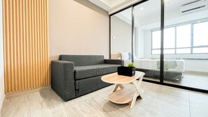 Una sala moderna con un sofá gris, una mesita redonda con una planta y un ventanal que ofrece vistas a otra habitación.