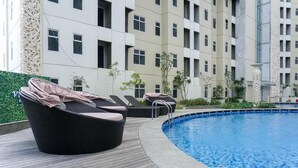 A pool area with lounge chairs and a modern building in the background. - Affordable Price 1Br Apartment At Vittoria Residence (Jakarta)