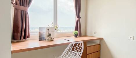 A room with a desk, a chair, a window with curtains, a small plant, and a bookshelf.