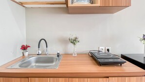 Μια κουζίνα με έναν ανοξείδωτο νεροχύτη, μια μαύρη βρύση, ένα μικρό φυτό σε γλάστρα, ένα βάζο με λουλούδια και μια καφετιέρα πάνω στον πάγκο.