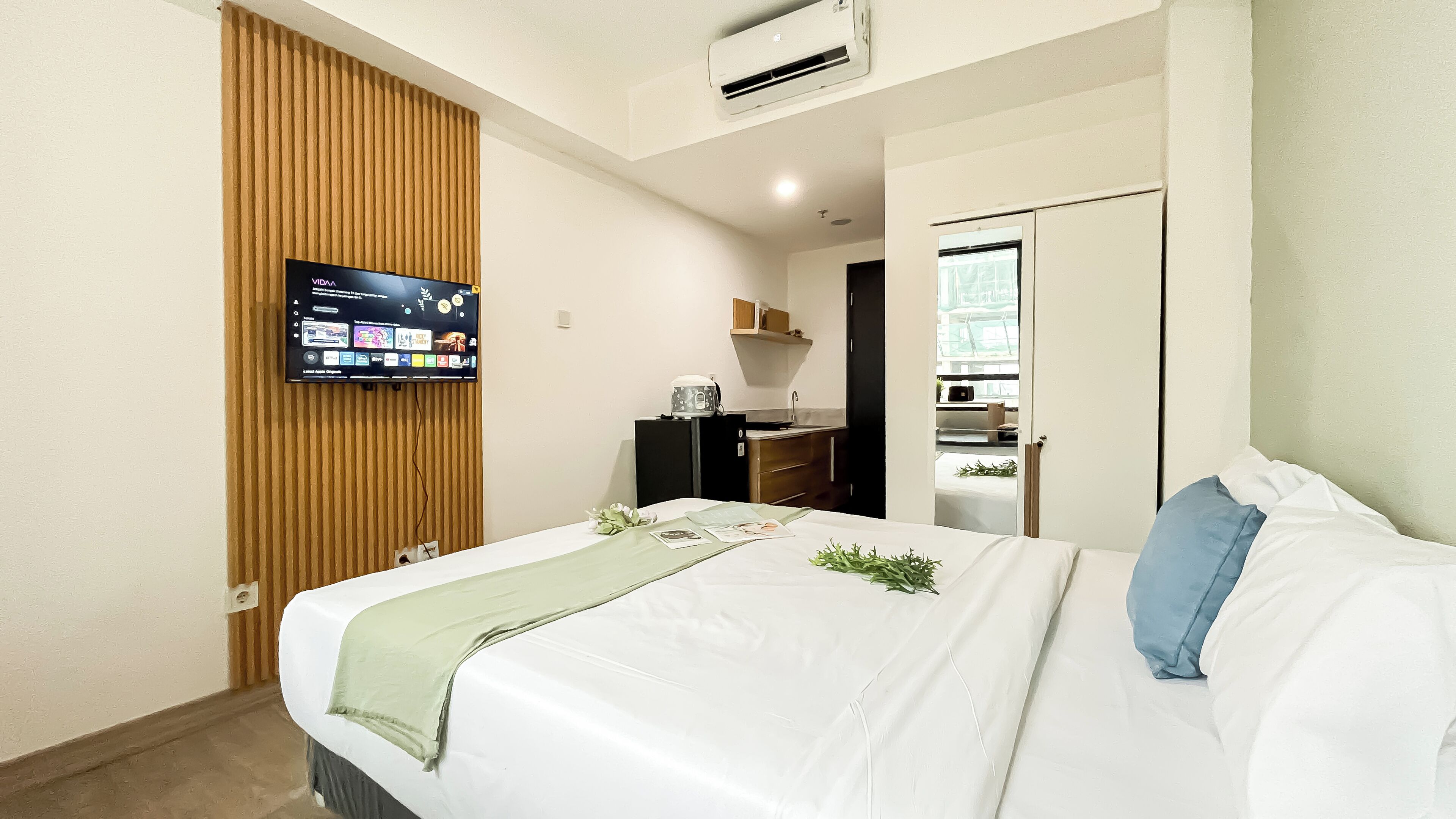 Hotelkamer met een bed, een televisie bevestigd aan een houten paneel, een kitchenette en een badkamer door een open deur zichtbaar.