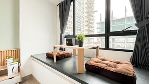 Una habitación moderna con ventana, una mesita pequeña, una planta en maceta y un pouf marrón.