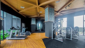 Un gimnasio con cintas de correr, máquinas de pesas y piso de madera.