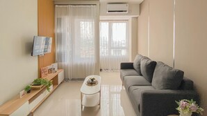 A modern living room with a grey sofa, a white coffee table, and a TV mounted on the wall. - Standard 2Br Near Station At Nifarro Park Apartment (Jakarta)