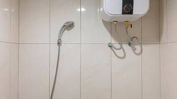 Un baño con pared de azulejos blancos, ducha de mano y calentador de agua eléctrico.