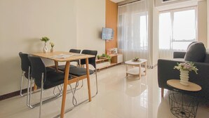 A modern living room with a dining area, a TV mounted on the wall, and a large window with sheer curtains. - Standard 2Br Near Station At Nifarro Park Apartment (Jakarta)