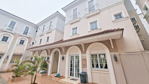 A multi-story building with a courtyard featuring palm trees, a trash bin, and a blue trash bin labeled "VETRA." - Modern 4Br Apartment At Guest House Vanya Park (Pagedangan)