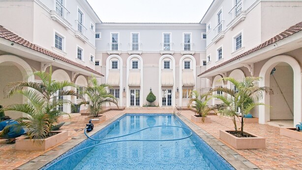 A swimming pool surrounded by white buildings with arched doorways and tiled roofs. - Modern 4Br Apartment At Guest House Vanya Park (Pagedangan)